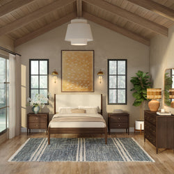 Modern rustic bedroom interior — mid-century wooden platform bed with upholstered headboard, vaulted wood-beam ceiling, black-framed windows, matching nightstands, blue striped area rug, fiddle leaf fig plant and warm neutral decor