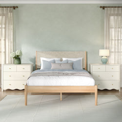 Modern cozy bedroom with soft green accent wall, light wood bed frame, matching nightstands, lamp, vase of white hydrangeas and sheer curtains