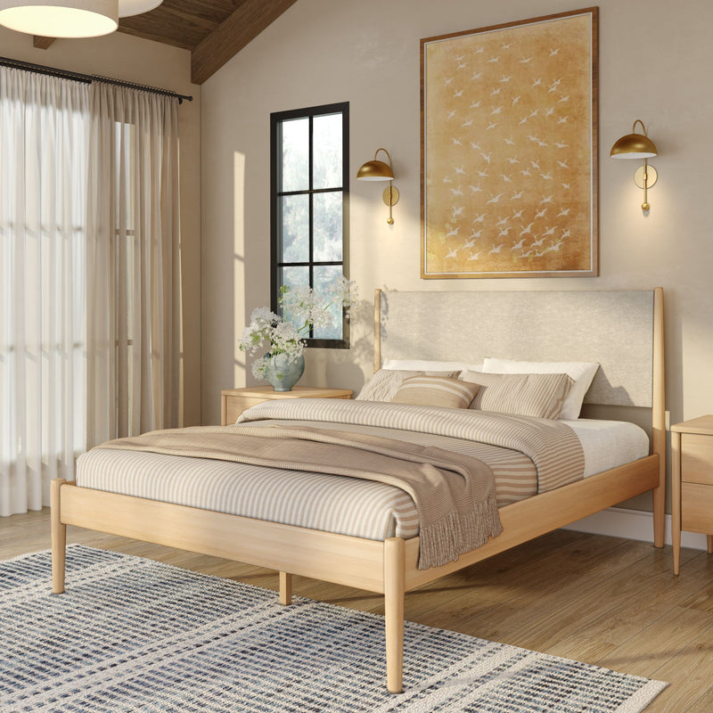 Cozy modern bedroom with light wood platform bed, striped beige bedding and throw, neutral decor, gold wall sconces, large framed artwork, sheer curtains and patterned rug
