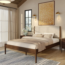 Modern cozy bedroom with walnut mid-century bed frame, neutral striped bedding and throw, blue patterned area rug, brass wall sconces and natural light
