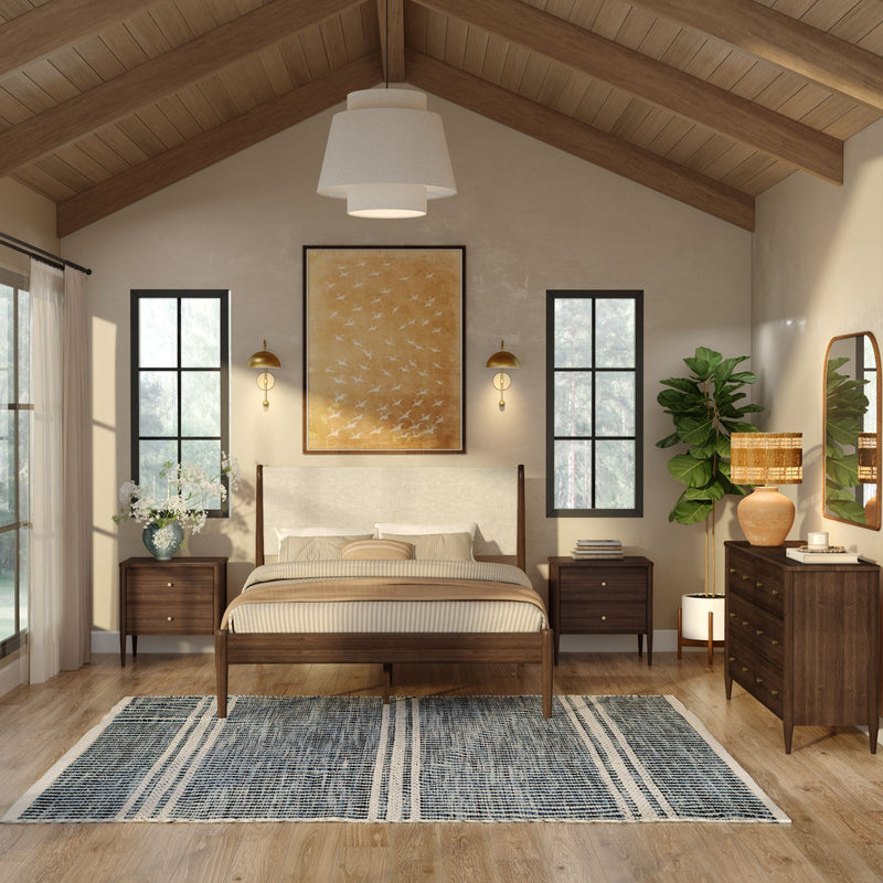 Modern farmhouse bedroom interior with vaulted wood ceiling, wooden bed frame, neutral bedding, brass wall sconces, large windows, woven blue rug, wooden dresser and potted fiddle leaf fig plant