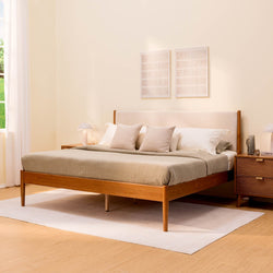 Mid-century modern wooden platform bed with beige linen bedding and upholstered headboard, matching nightstands, area rug and natural light in minimalist bedroom