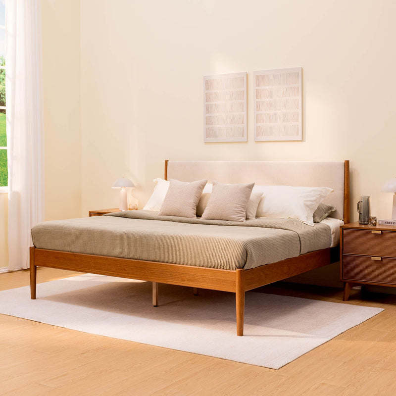 Mid-century modern wooden platform bed with beige linen bedding and upholstered headboard, matching nightstands, area rug and natural light in minimalist bedroom