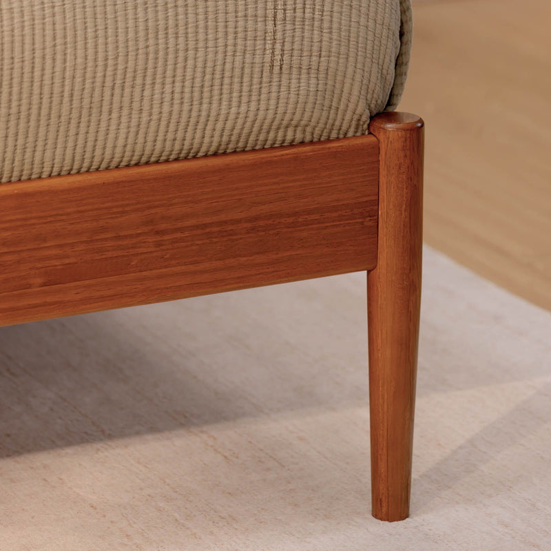 Close-up of solid wood mid-century modern bed frame leg and side rail with beige quilted bedding on a light area rug