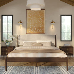Modern neutral bedroom with a wooden mid-century bed frame, striped beige bedding, matching nightstands, brass wall sconces, large framed bird artwork and black-framed windows