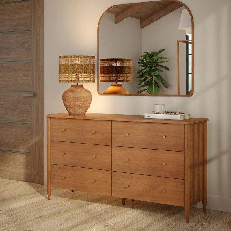 Mid-century modern six-drawer wooden dresser with brass knobs, terracotta lamp with woven shade, arched wall mirror and fiddle-leaf fig plant in a minimalist wood-floor entryway