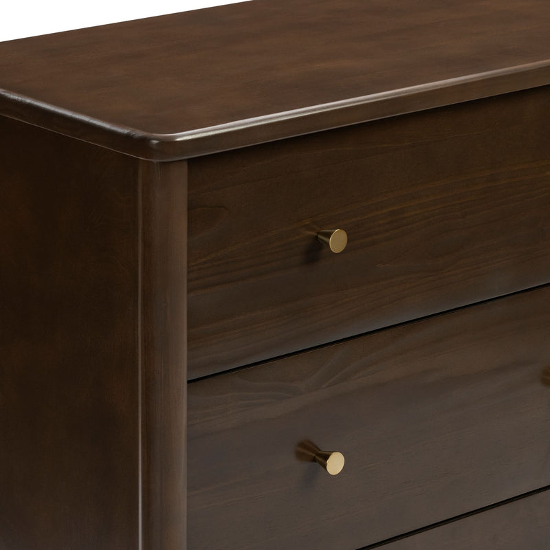Close-up of dark walnut wooden dresser with smooth beveled edge and brass round knobs, modern mid-century bedroom storage furniture