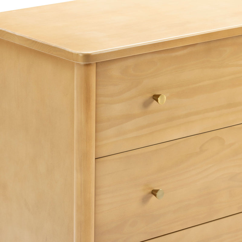 Close-up of minimalist light wood dresser with natural pine finish and brass round drawer knobs, modern bedroom storage furniture