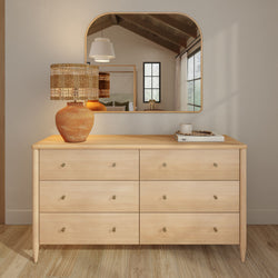 Minimalist six-drawer light wood dresser with terracotta lamp and woven shade, books and arched mirror in a Scandinavian-modern bedroom setting