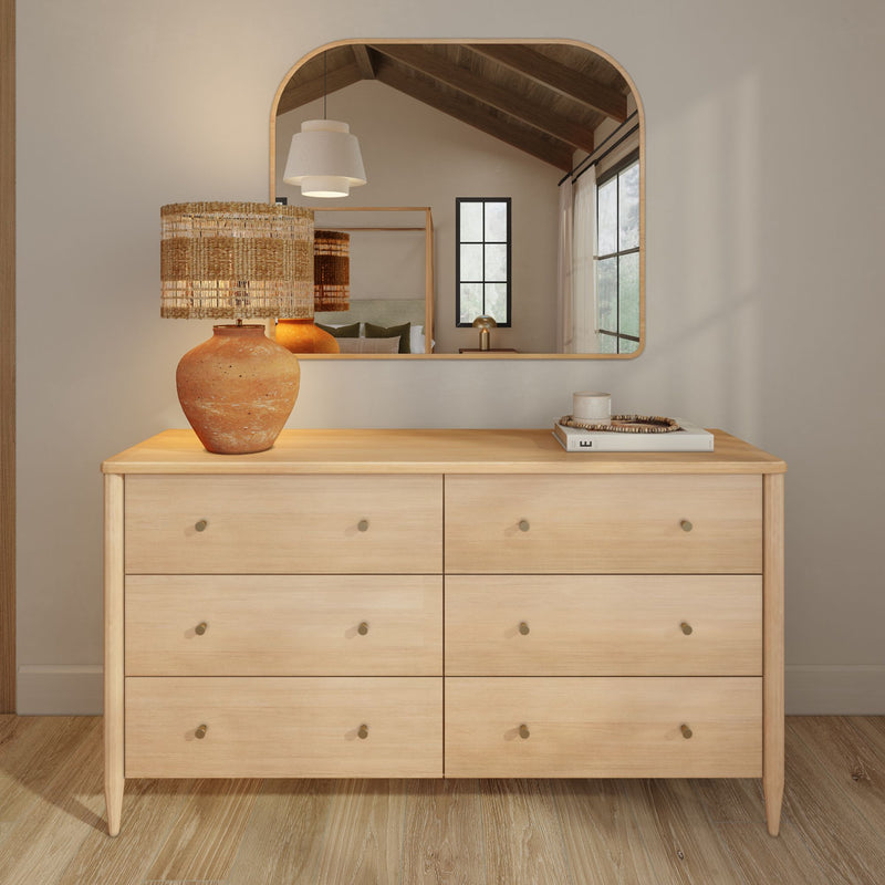Minimalist six-drawer light wood dresser with terracotta lamp and woven shade, books and arched mirror in a Scandinavian-modern bedroom setting
