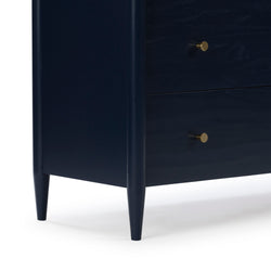 Close-up of navy blue wooden dresser corner with tapered mid-century legs, two drawers and round brass knobs on white background