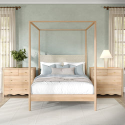 Light wood four-poster canopy bed in modern coastal bedroom with matching nightstands, linen bedding, blue pillows, potted plant and sheer curtains
