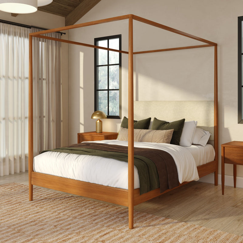 Modern wooden four-poster canopy bed in neutral bedroom with linen bedding, green and brown throws, gold bedside lamp, mid-century nightstands, sheer curtains and warm natural light