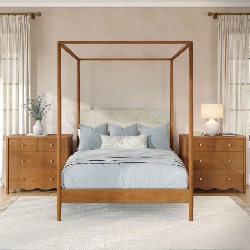 Wooden four‑poster canopy bed in a neutral modern farmhouse bedroom with light blue bedding, matching wooden nightstands with brass knobs, ceramic table lamps, eucalyptus vase and sheer curtains