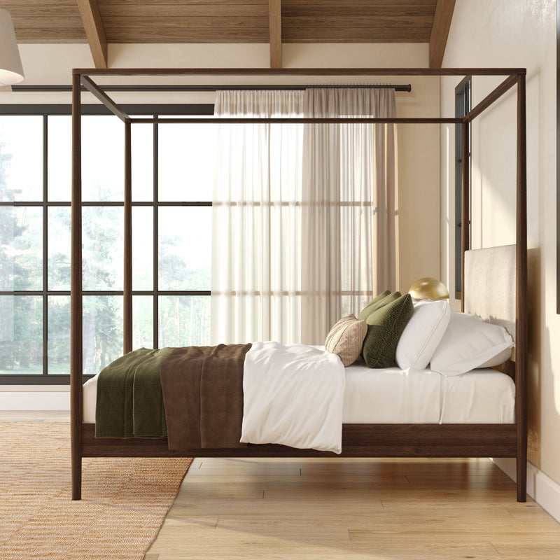 Sunlit modern bedroom with dark wood four-poster bed, white linens, green and brown throw blankets and pillows, sheer curtains and large black-framed windows on light hardwood floor