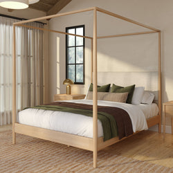 Minimalist Scandinavian bedroom with light wood four‑poster canopy bed, white linen bedding, green and brown throws, nightstand with brass lamp