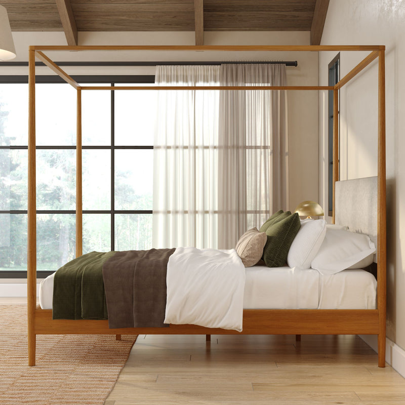 Modern wooden four-poster canopy bed with neutral linen, green accent pillows, hardwood floors and large window with sheer curtains