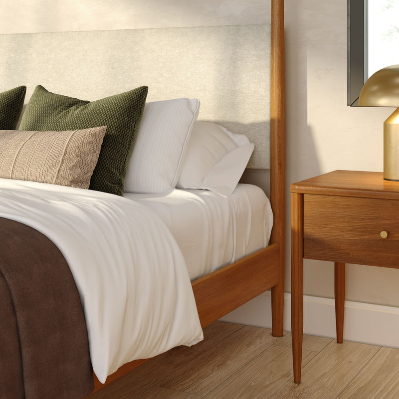Mid-century modern bedroom corner with wooden bed frame, white linen bedding, green and beige throw pillows, wood nightstand and gold lamp