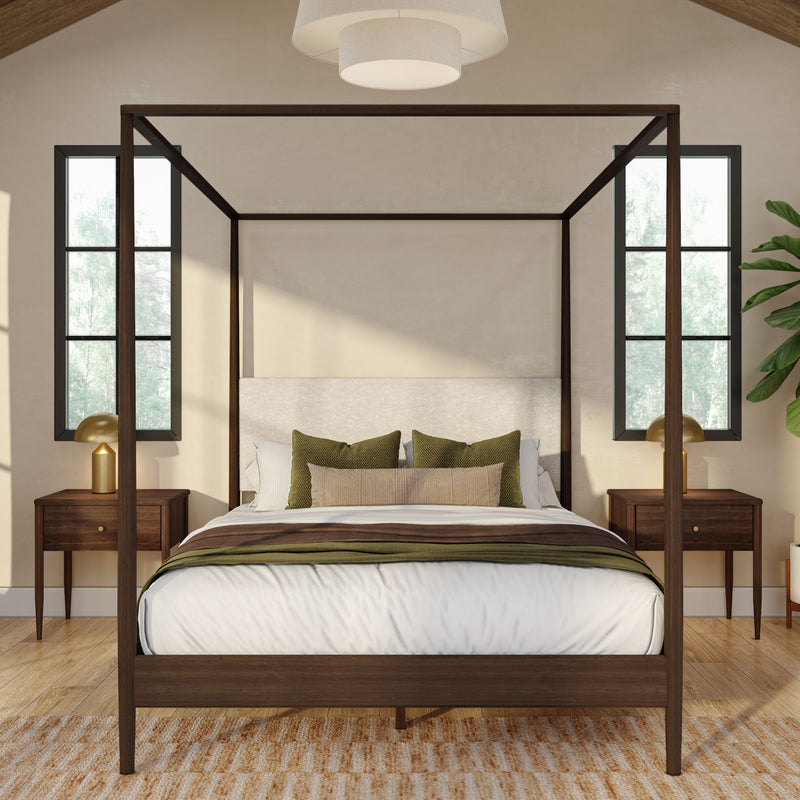 Wooden four-poster bed in neutral bedroom with olive-green pillows, mid-century nightstands, brass lamps and natural light