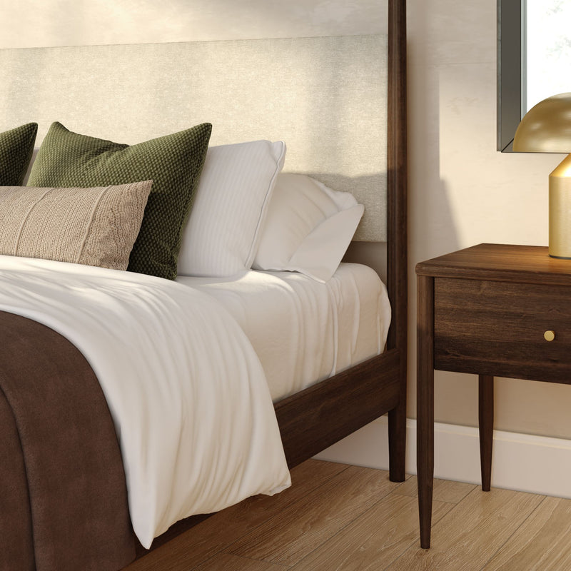 Cozy modern bedroom corner with wooden bed frame, white bedding, green and beige accent pillows and walnut nightstand with gold lamp.