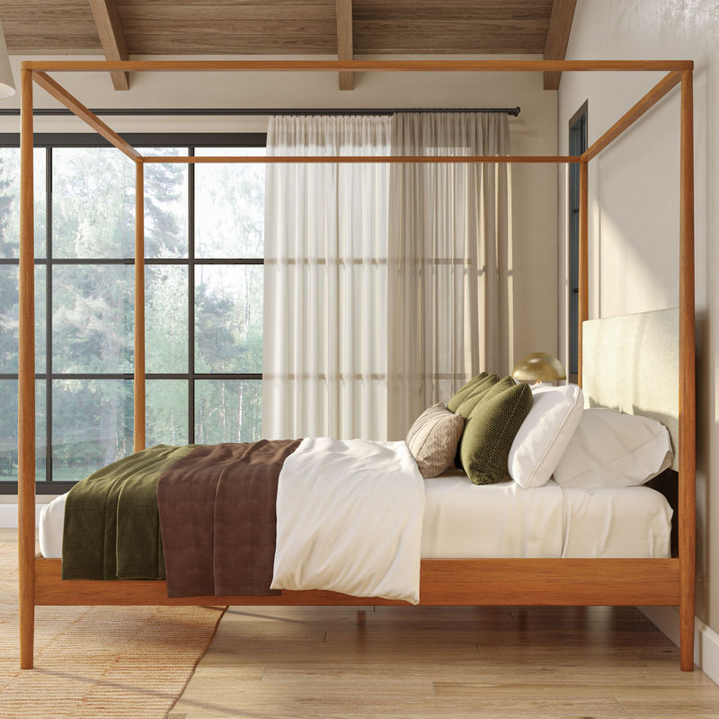 Modern rustic bedroom featuring a wooden four‑poster bed with white linens, brown and olive green throw blankets and pillows, sheer curtains, and large floor‑to‑ceiling windows overlooking a forest, flooded with natural light