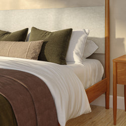 Modern wooden platform bed with upholstered headboard, white linens, olive green textured pillows, beige lumbar pillow and brown throw blanket beside a wooden nightstand