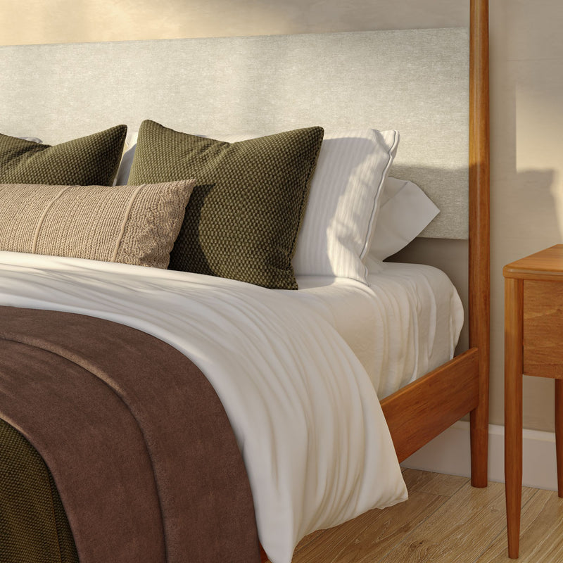 Modern wooden platform bed with upholstered headboard, white linens, olive green textured pillows, beige lumbar pillow and brown throw blanket beside a wooden nightstand