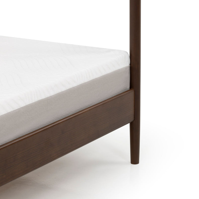 Close-up of bed corner showing a white mattress topper and beige base on a dark walnut mid-century modern wooden bed frame