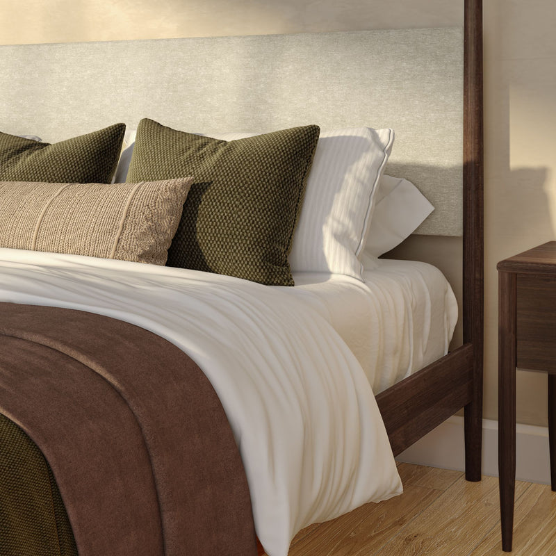 Modern bedroom close-up: layered neutral bedding with olive green textured pillows, beige upholstered headboard, wooden bed frame and nightstand on hardwood floor