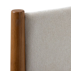 Close-up of rounded walnut wood bedpost and cream bouclé upholstered headboard, mid-century modern furniture detail
