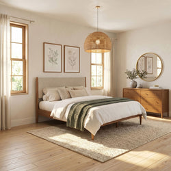 Cozy modern boho bedroom interior with rattan pendant lamp, wooden bed frame, neutral bedding and green knit throw, hardwood floors, dresser with round mirror and botanical prints