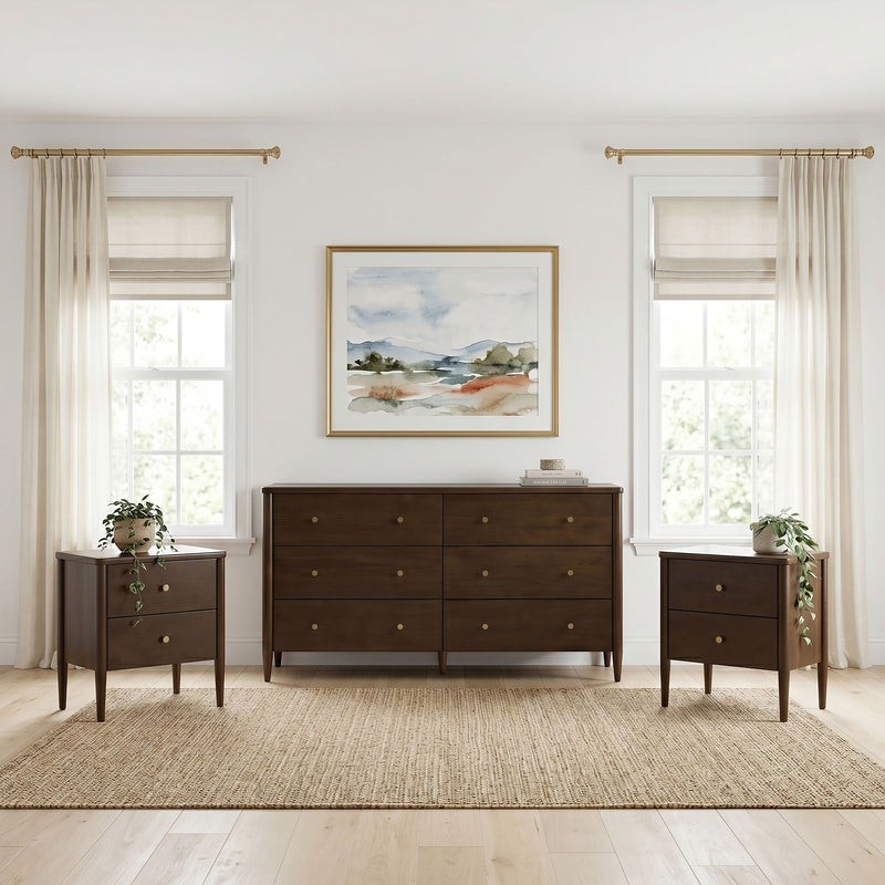 Dark wood mid-century dresser with matching nightstands and potted plants, framed watercolor art between two windows with sheer curtains, beige Roman shades and brass curtain rods, neutral modern bedroom decor