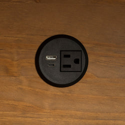 A close-up of a black electric socket with a USB-A port, USB-C port, and standard American socket. 