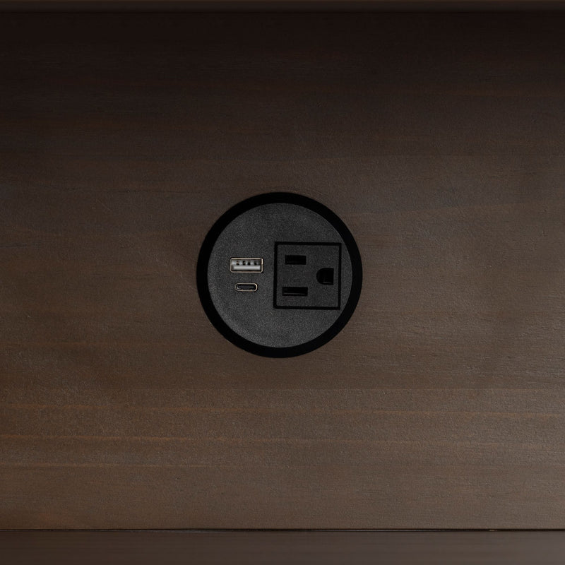 Round recessed power outlet with AC socket, USB-A and USB-C charging ports mounted in dark wood desk.
