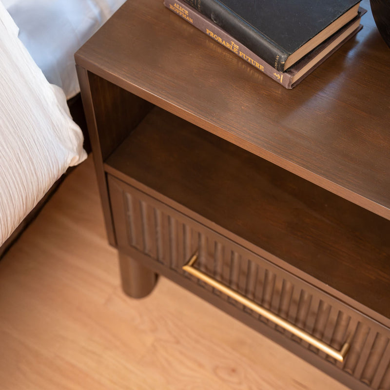 Close-up of a modern walnut nightstand bedside table with brass handle, open shelf and stacked books on a light hardwood bedroom floor