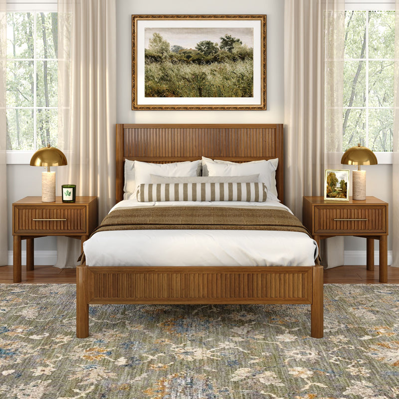 Mid-century modern wooden bed in a neutral master bedroom with striped bolster pillow, matching nightstands and brass lamps, landscape wall art and patterned area rug