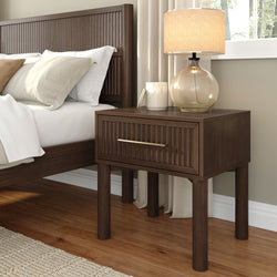 Modern bedroom close-up of dark wood ribbed nightstand with brass-handle drawer, glass table lamp and neutral linen pillows