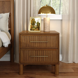 Wooden nightstand with ribbed drawers topped by a stone-base table lamp with gold dome shade and a framed landscape painting, next to a wooden bed and beige curtains — cozy modern bedroom decor