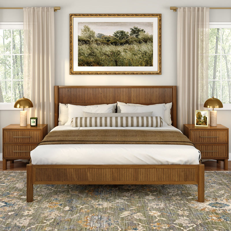 Modern bedroom interior with wooden bed frame, neutral bedding and striped bolster, wood nightstands, gold lamps, framed landscape art and patterned area rug