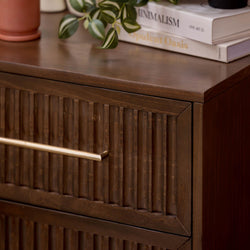 Dark walnut mid-century modern dresser with fluted drawer fronts and brass handle, styled with a potted plant and stacked decor books on top