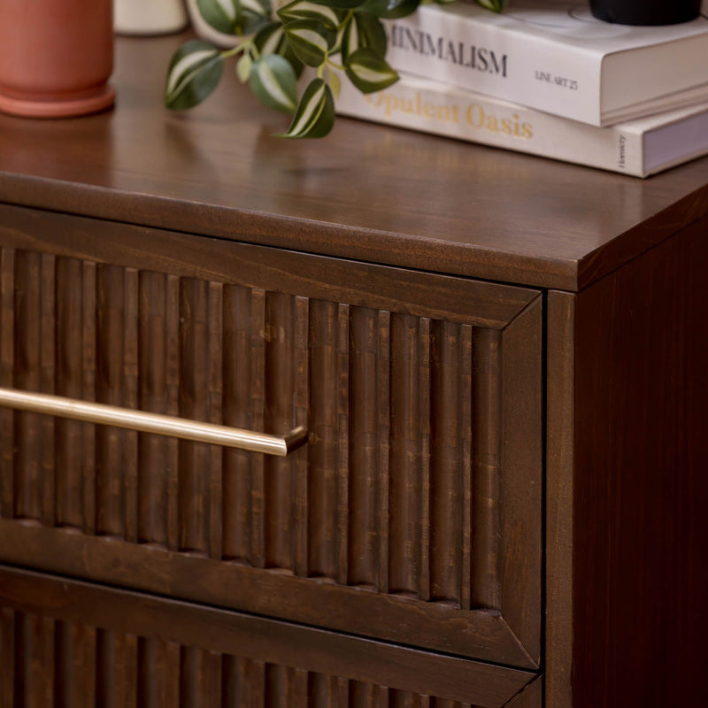 Dark walnut mid-century modern dresser with fluted drawer fronts and brass handle, styled with a potted plant and stacked decor books on top