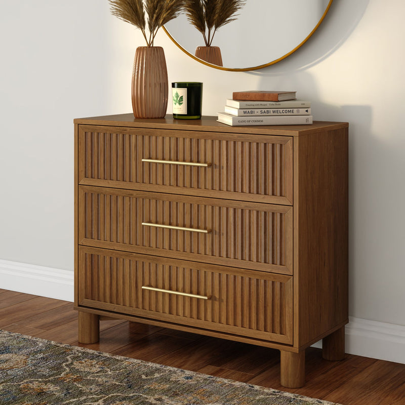 Mid-century wooden dresser with fluted drawer fronts and brass handles, styled with a vase of pampas grass, green candle, stacked books and round wall mirror