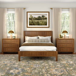 Modern neutral bedroom with mid-century wooden bed frame, matching bedside dressers, patterned area rug, striped bolster pillow, sheer curtains, gold table lamps and framed landscape artwork centered between two tall windows