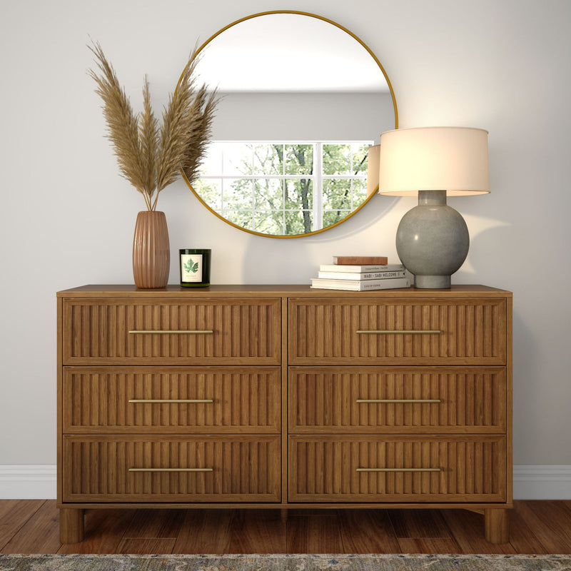 Natural wood six-drawer dresser with fluted fronts and brass handles styled with round gold-framed mirror, gray ceramic table lamp, terracotta vase with pampas grass and scented candle, modern entryway decor