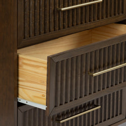 Dark brown wooden dresser with ribbed drawer fronts and brass bar handles, open drawer revealing light pine interior — modern bedroom storage