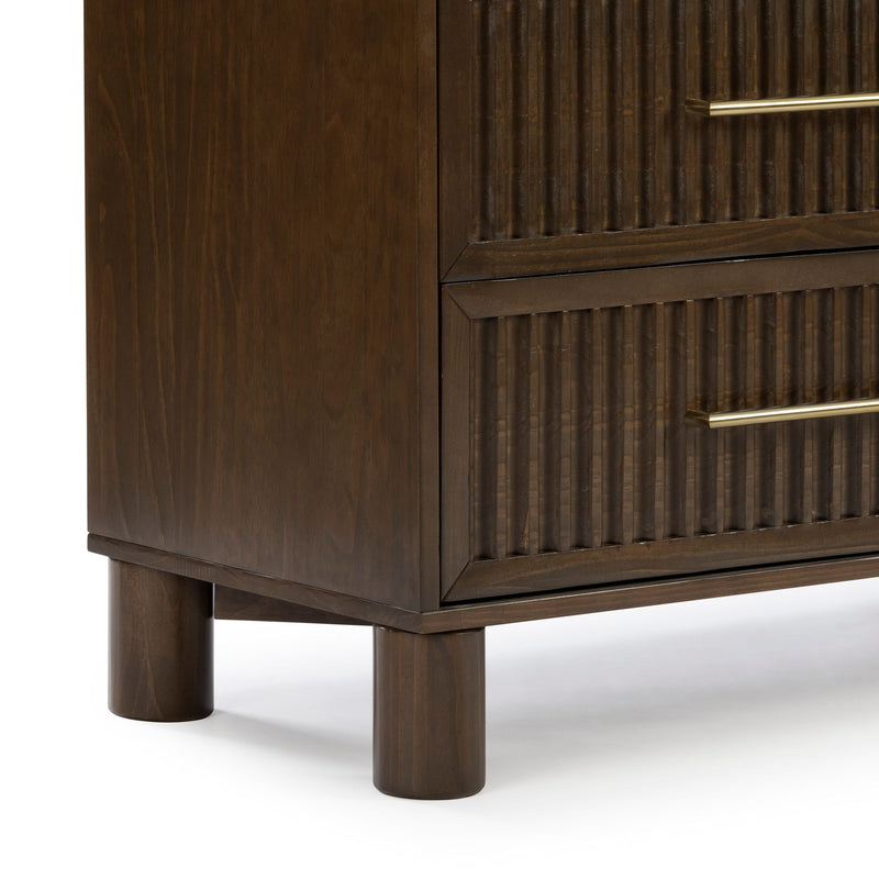 Close-up of dark walnut wood dresser corner with fluted drawer fronts, brass bar handles and round cylindrical legs — mid-century modern bedroom furniture