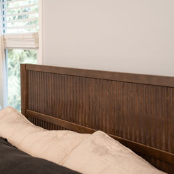 Textured wooden headboard with vertical grooves in a modern neutral bedroom, beige quilted bedding and window blinds letting in natural light