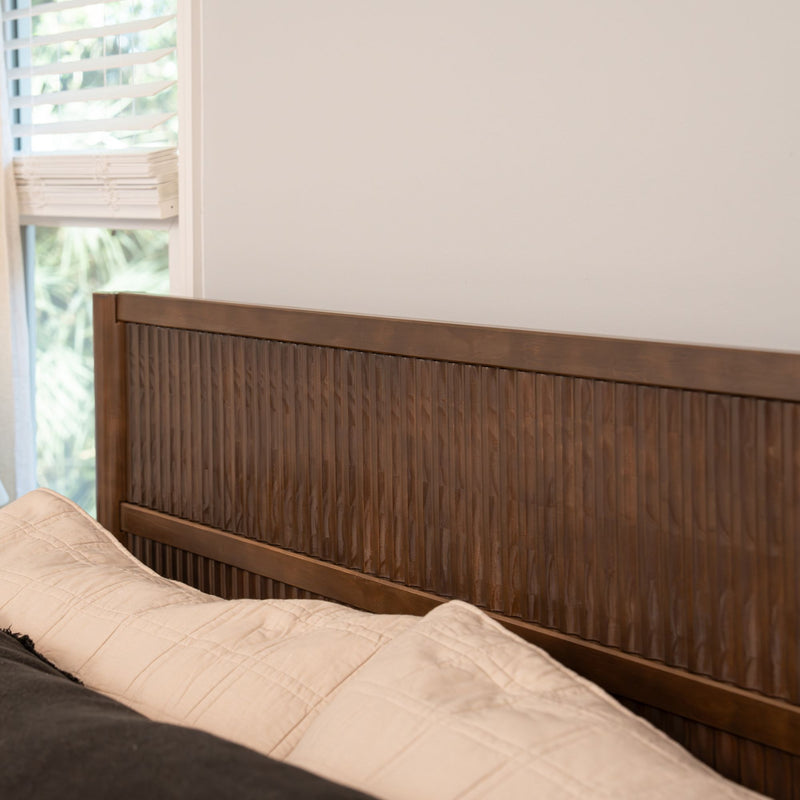 Textured wooden headboard with vertical grooves in a modern neutral bedroom, beige quilted bedding and window blinds letting in natural light