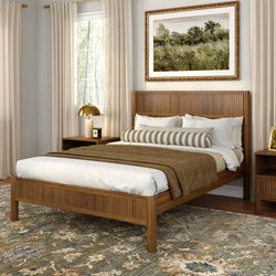 Cozy modern bedroom with wooden slatted bed frame, neutral bedding and striped bolster pillow, gold bedside lamp, framed landscape art, sheer beige curtains and patterned area rug