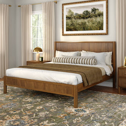Modern bedroom with wooden slatted bed frame, neutral bedding and striped bolster, textured earth-tone area rug, framed landscape wall art, gold bedside lamp and sheer curtains